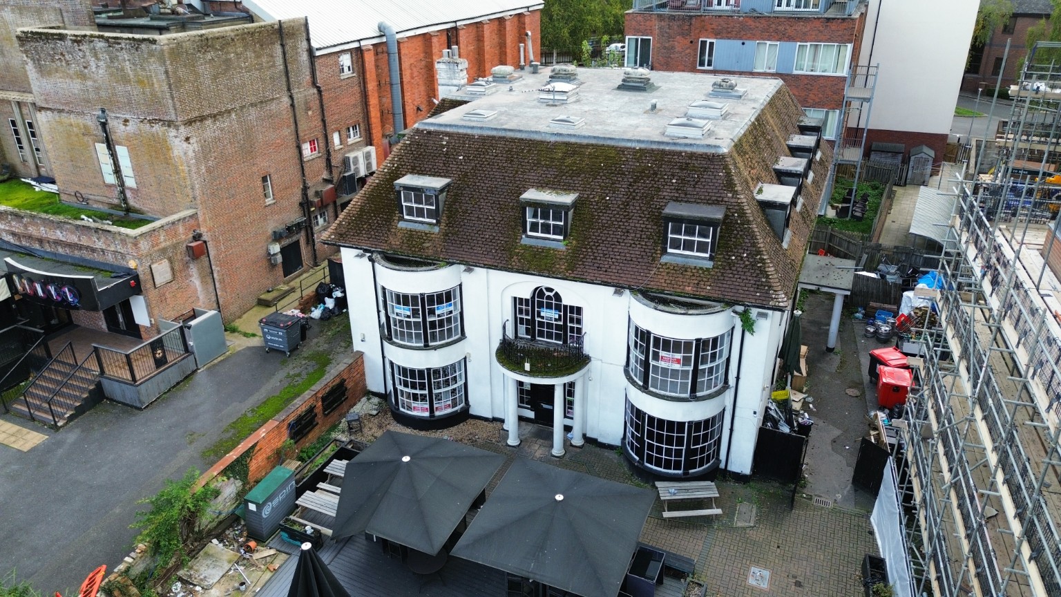 Drone view of a commercial building with outdoor seating and neighbouring buildings